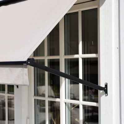 Utdragen markis i tyg och metallstomme, fotograferad i solljus vid ett fönster.