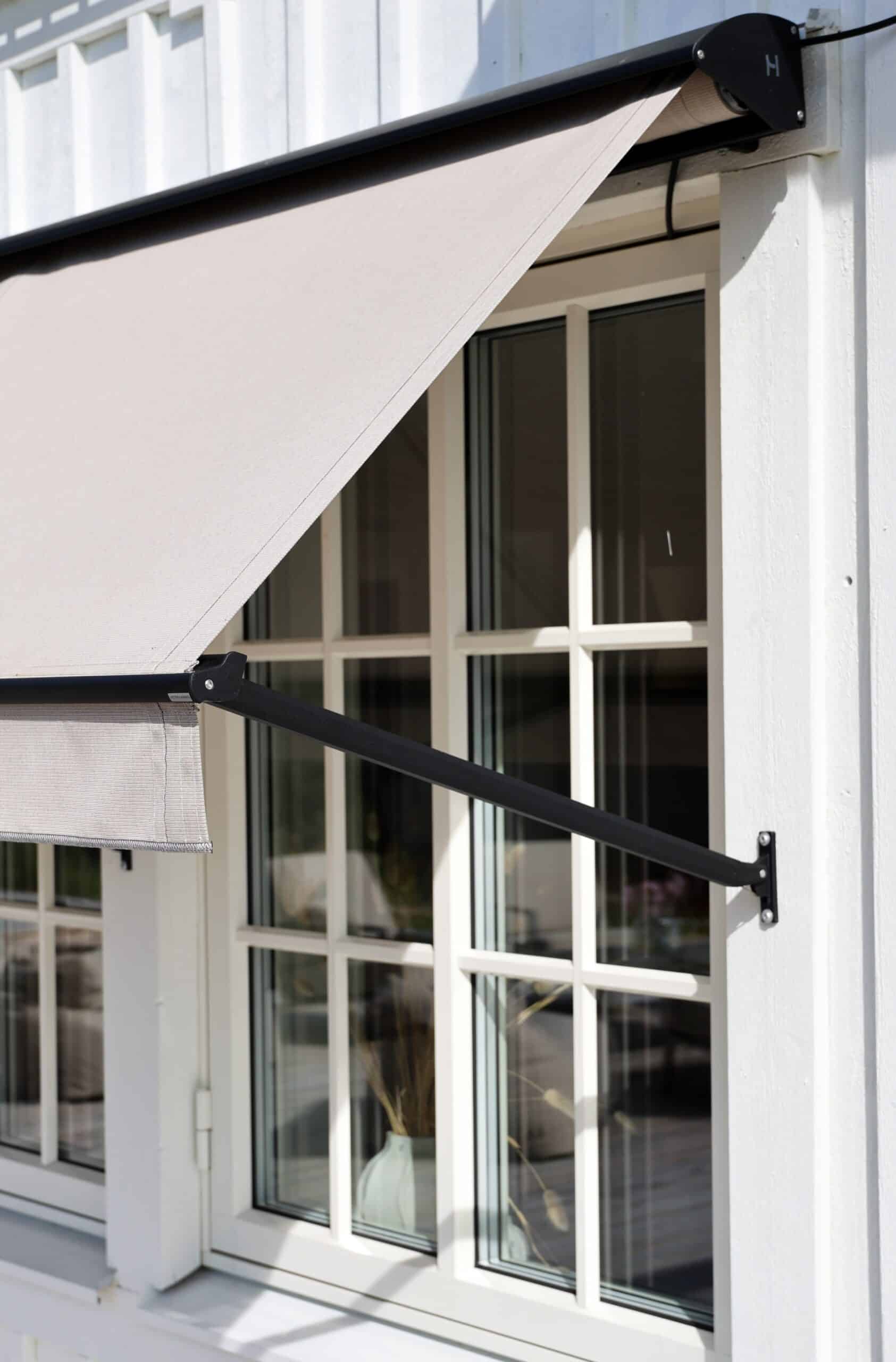 Utdragen markis i tyg och metallstomme, fotograferad i solljus vid ett fönster.