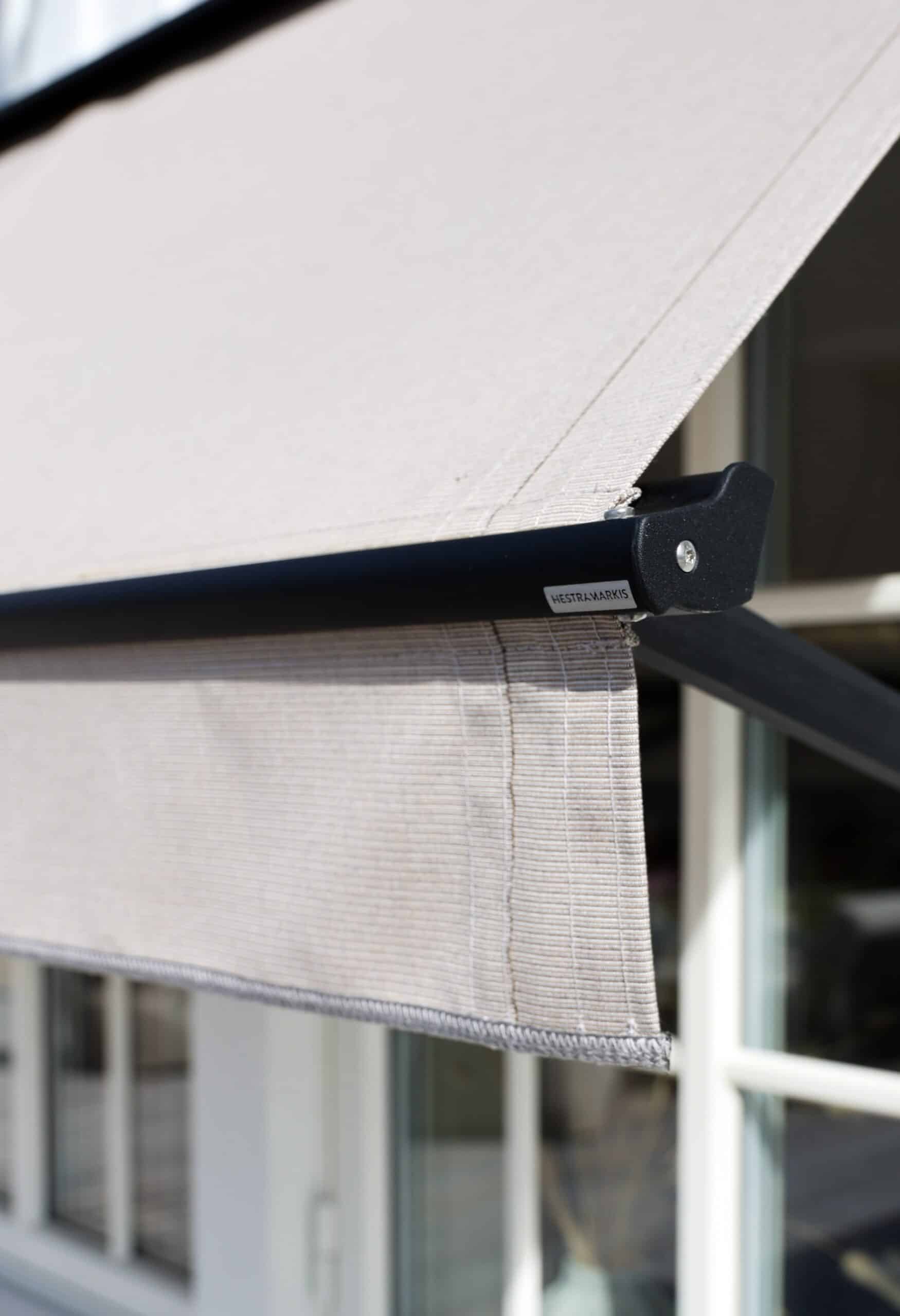 Detaljvy av en fönstermarkis i ljusgrått tyg med synliga sömmar och metallarm.