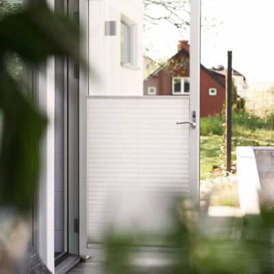 Ljusinsläpp genom dörr med vit plisségardin.