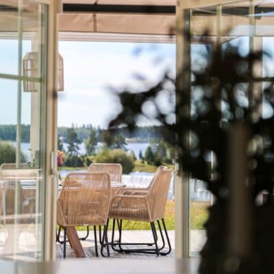 Uteplats med markis och rottingmöbler, vy mot sjön.