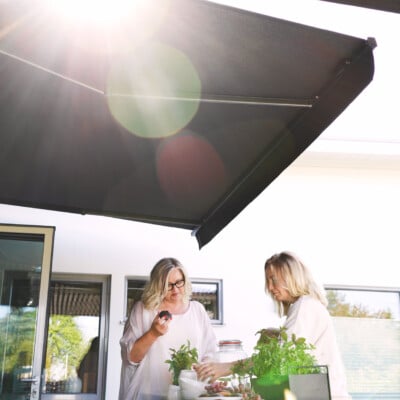 Två personer under svart terrassmarkis i solljus