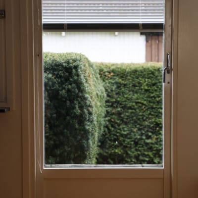 Persienner i balkongdörr med trädgårdsutsikt.