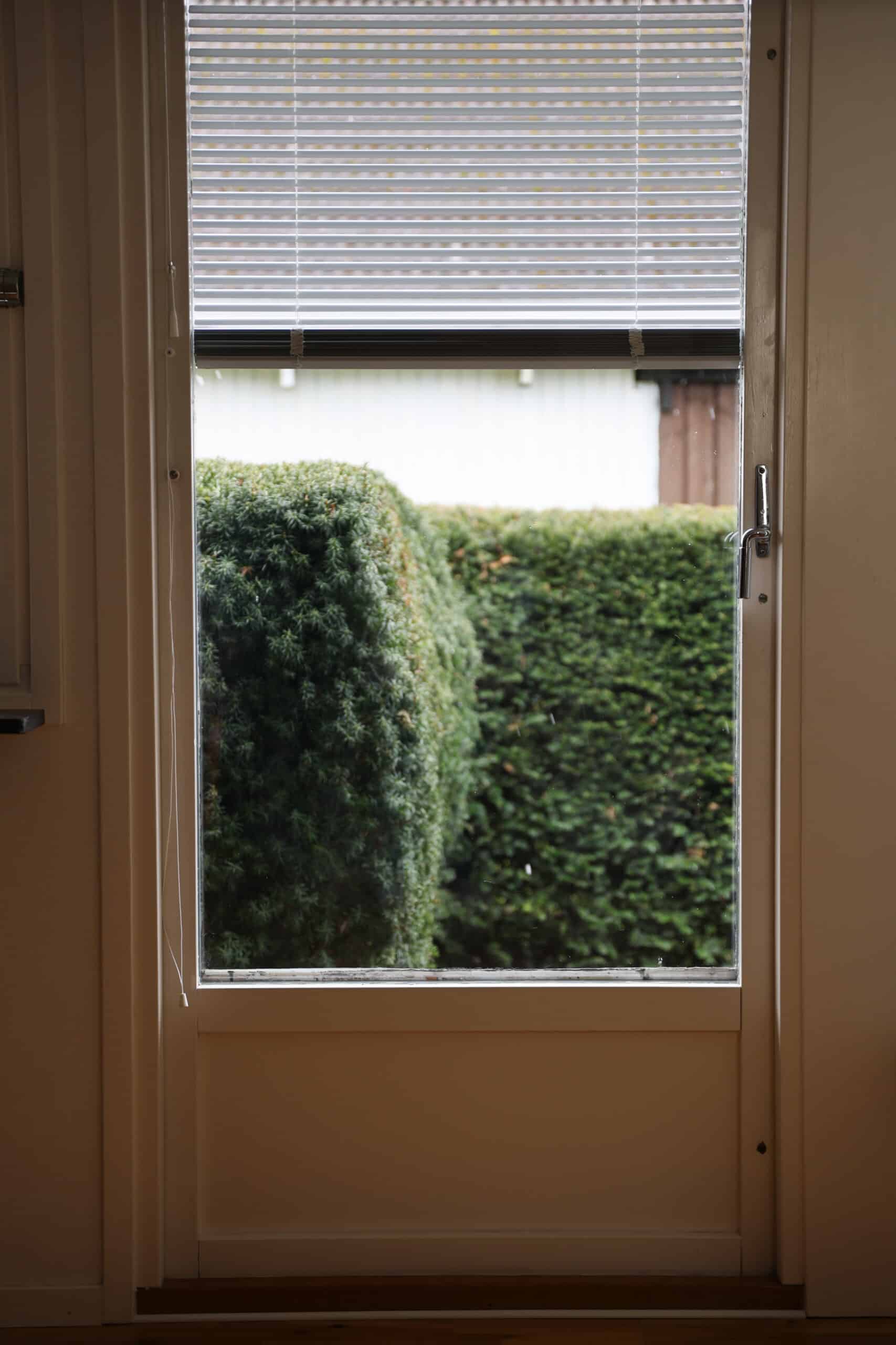 Persienner i balkongdörr med trädgårdsutsikt.