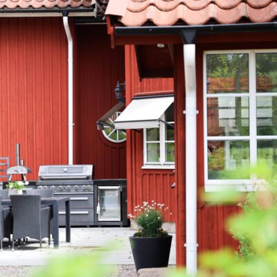 Rött trähus med vita markiser och uteplats med grill