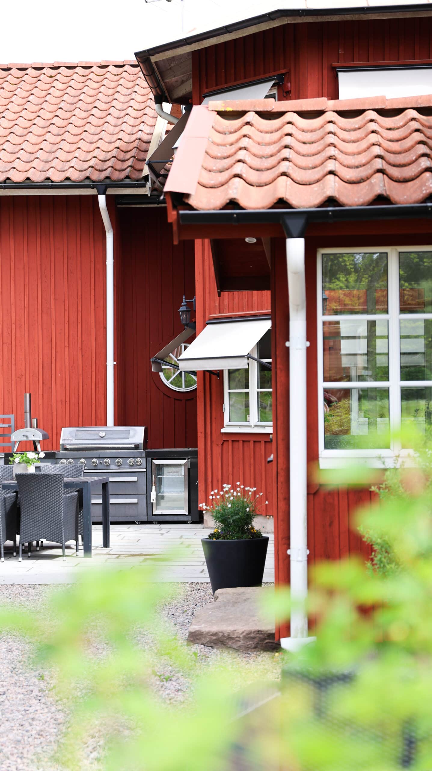 Rött trähus med vita markiser och uteplats med grill