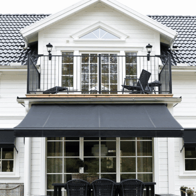 Vit villa med svart terrassmarkis över glasdörrar.