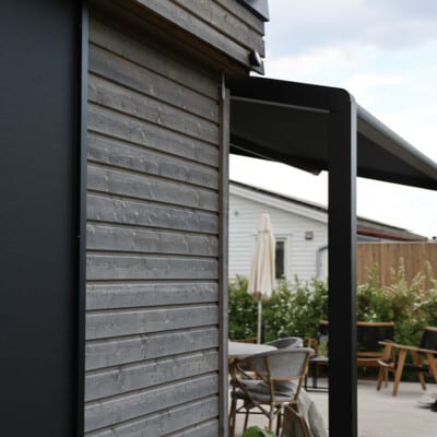 Pergolamarkis vid uteplats med trämöbler och parasoll.